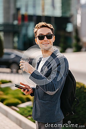 Young Cheerful man in city drinking cup of coffee to go and looking somewhere Stock Photo