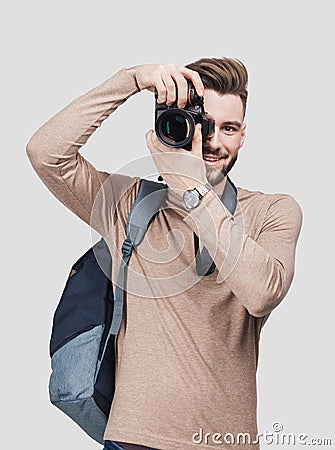 Young cheerful man photographer takes images with digital camera. Isolated on gray background Stock Photo