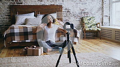 Young cheerful mixed race girl recording video blog about packing christmas gift box at home Stock Photo