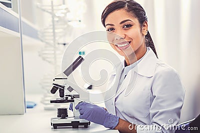 Young chemist wearing white uniform sitting near microscope Stock Photo