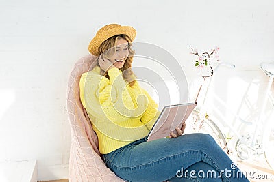 Young girl in straw hat sitting reading book on veranda in wicker chair smiling happily hobby pastime concept Stock Photo