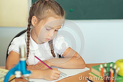 Young child girl drawing or writing with colorful pencils in notebook in school over blackboard Stock Photo