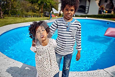 Young children by the pool, african american borther and sister acting silly making faces together standing by the pool outdoors Stock Photo