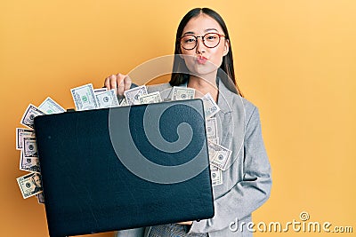 Young chinese woman holding briefcase full of dollars looking at the camera blowing a kiss being lovely and sexy Editorial Stock Photo