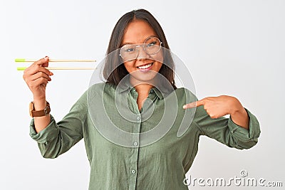 Young chinese woman wearing glasses holding chopsticks over isolated white background with surprise face pointing finger to Stock Photo