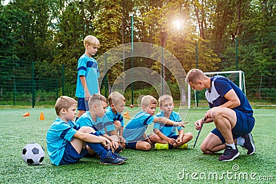 Young coach teaches little children the strategy of playing on football field. Stock Photo