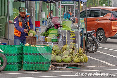 A young coconut seller without masker is peeling coconuts on a hot day, in the area around Simpang Lima, Boyolali City. BOYOLALI Editorial Stock Photo