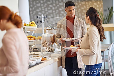 Young colleagues talking while picking a food at company canteen. People, job, company, business concept Stock Photo