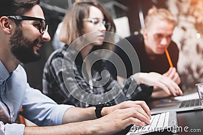 Young company of creative men and women working for modern devices in loft space. Coworking team is working on new idea and Stock Photo