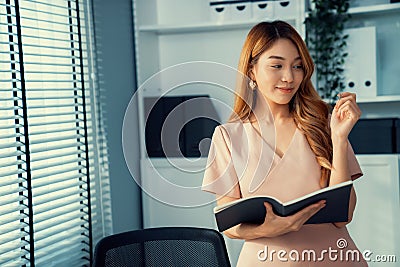 Young competent office lady, intern, secretary holding a log in office room. Stock Photo