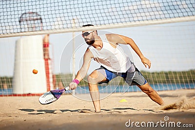 Young competetive man, athlete in singlasses playing paddle tennis, training outdoors on warm summer evening. Match Stock Photo