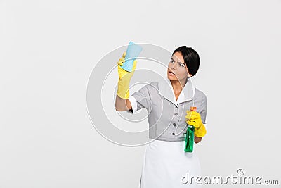 Young concentrated maid in uniform cleaning window with rag Stock Photo