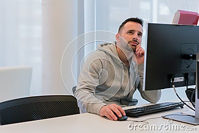 Young concentrated man thinking about the answer of the questions in front of the computer screen Stock Photo