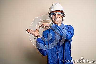 Young constructor man wearing uniform and security helmet over isolated white background amazed and smiling to the camera while Stock Photo
