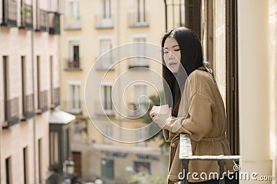 Young contemplative and beautiful Asian woman at home or hotel balcony - thoughtful Korean girl having morning coffee enjoying Stock Photo