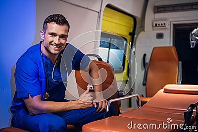 Young corpsman in blue medical uniform sits in the ambulance car and smiles Stock Photo