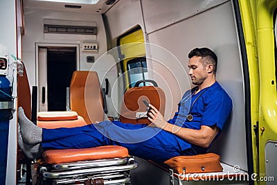 Young corpsman in uniform sits with phone in the ambulance car Stock Photo