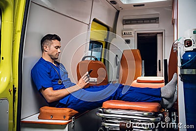 Corpsman in blue medical uniform sits with phone in the ambulance car Stock Photo