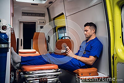 Young corpsman in uniform sits with phone in the ambulance car Stock Photo