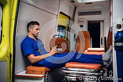 Young corpsman sitting with his phone in the ambulance car Stock Photo