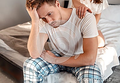 Young couple in the bed. Close-up of unhappy man is sitting on the edge of bed, problem in the bedroom Stock Photo