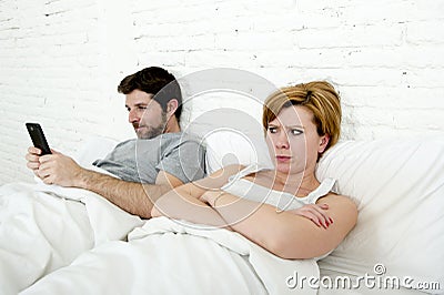 young couple in bed unsatisfied wife bored frustrated and angry while internet addict husband is using mobile phone social networ Stock Photo