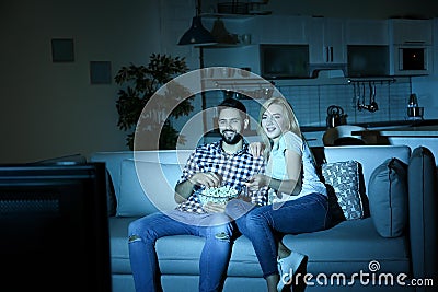 Young couple with bowl of popcorn watching TV on sofa Stock Photo