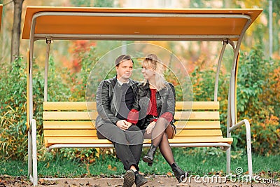 A young couple-brown-haired and blonde-sit on a bench and hold hands Stock Photo