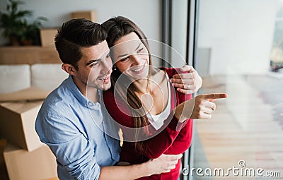 Young couple with cardboard boxes moving in a new home, looking out of window. Stock Photo
