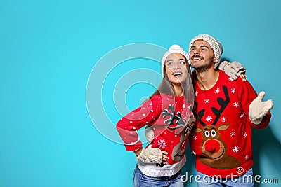 Young couple in Christmas sweaters and knitted hats on color background. Stock Photo