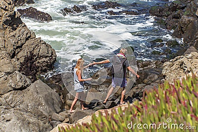 Young couple climbing the rocks and enjoying the view along the rugged Big Sur coastline. Stock Photo