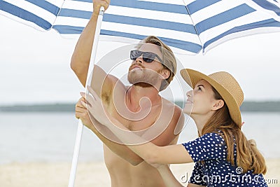 young couple erecting parasol on beach Stock Photo