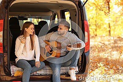 Young couple with guitar sitting in open car trunk Stock Photo