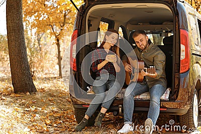 Young couple with guitar sitting in open car trunk Stock Photo