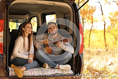 Young couple with guitar sitting in open car trunk Stock Photo
