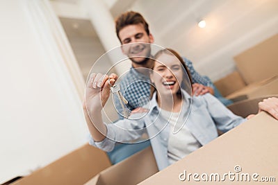 Young couple having fun while moving to new apartment. Moving newlyweds. Girl is sitting in a box. Stock Photo