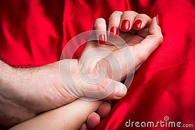 Young couple holding hands sensually on red silk bed Stock Photo