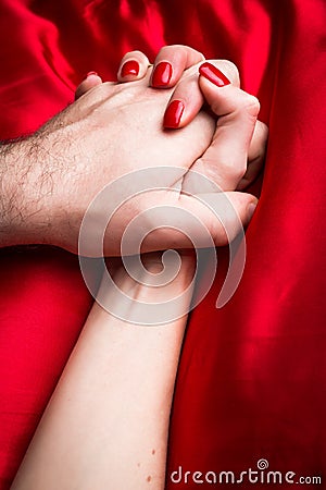Young couple holding hands sensually on red silk bed Stock Photo