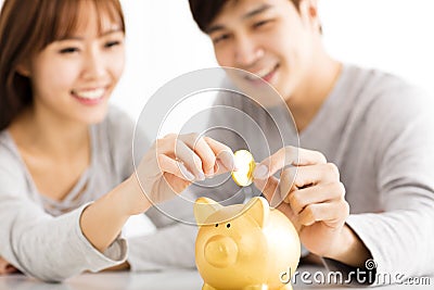 young Couple Inserting Coin In Piggybank Stock Photo