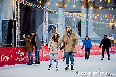 Young couple in love Caucasian man with blond hair with long hair and beard and beautiful woman have fun, active date skating on i Editorial Stock Photo