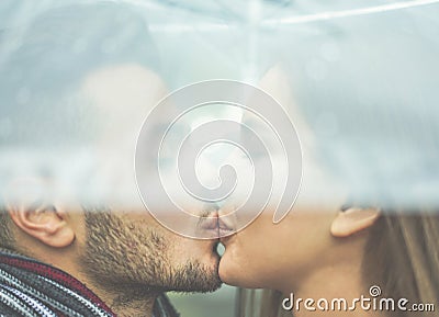 Young couple in love kissing under the rain with transparent umbrella - Handsome bearded man and woman enjoying havig tender Stock Photo