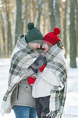 Young couple in love in snow-covered winter park covered themselves with warm blanket. Vertical frame Stock Photo
