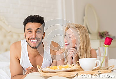 Young Couple Lying In Bed Eat Breakfast Morning With Red Rose Flower, Happy Smile Hispanic Man And Woman Stock Photo