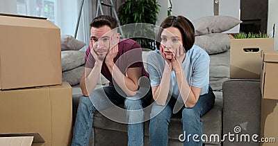 Young couple move into new apartment. Tired couple sit on sofa surrounded huge carton boxes. Feeling stressed moving Stock Photo