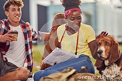 A young couple is posing for a photo while sitting on the grass in the park with their dogs. Friendship, rest, pets, picnic Stock Photo