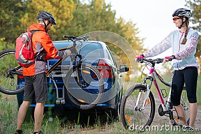 Young Couple Unmounting Mountain Bikes from Bike Rack on the Car. Adventure and Family Travel Concept. Stock Photo