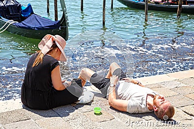 A young couple relax at the water`s edge near St. Mark`s Square in Venice Editorial Stock Photo