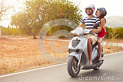 Young Couple Riding Motor Scooter Along Country Road Stock Photo