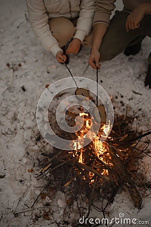 A young couple roast bread on a campfire in a snowy forest Stock Photo