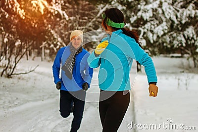 Young couple running dressed warmly in fleeces and gloves jogging in sunshine across winter snow Stock Photo